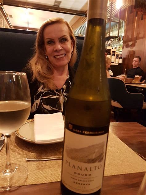 a woman sitting at a table with a bottle of wine in front of her and a glass of white wine
