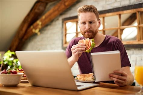Free Photo | Mid adult man eating sandwich while using laptop at dining table