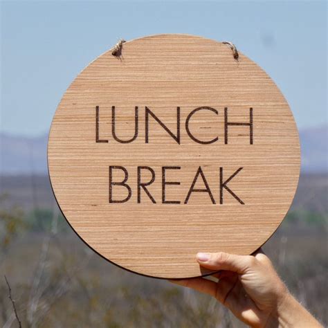 a person holding up a wooden sign that says lunch break in front of a desert landscape