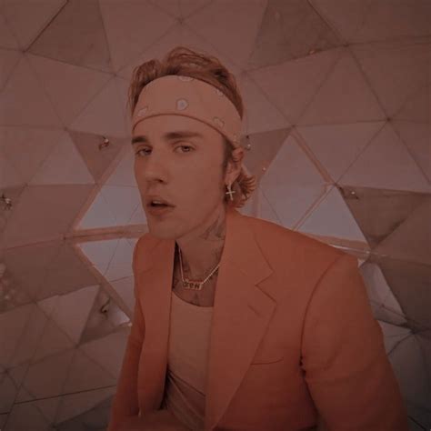a man in an orange jacket and headband standing next to a wall with geometric shapes