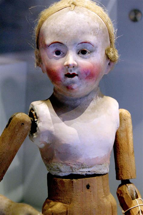 an old wooden doll with white paint on it's face and chest, holding a piece of wood in her hand