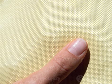 Finger on bulletproof material aramid. Shining aramid kevlar background. Yellow kevlar texture ...