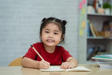 Asian Baby Girl Smiling Wearing a Red Shirt Write Notes in Notebook and Reading Book To Study ...