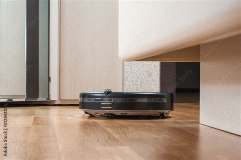 black Robot vacuum cleaner runs under bed on laminate floor in bedroom ...