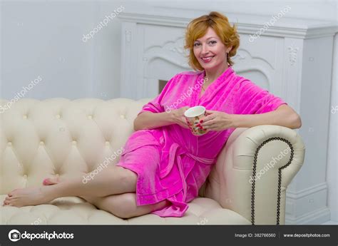 Beautiful young woman in a bathrobe relaxes on a sofa by the fireplace ...