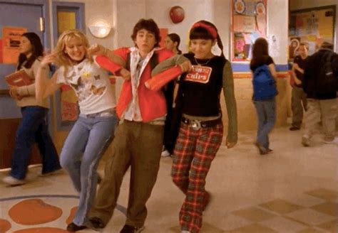 the young people are dancing together in the school hallway, with one girl wearing plaid pants