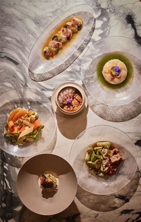 four plates with food on them sitting on a marble counter top in the middle of a table