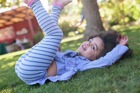 Portrait of young girl, lying on grass, legs raised - Stock Photo ...