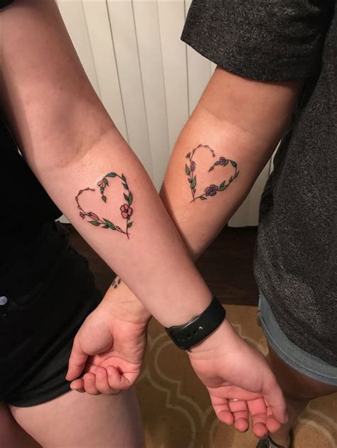 two people holding hands with tattoos on their arms and one has a heart in the middle