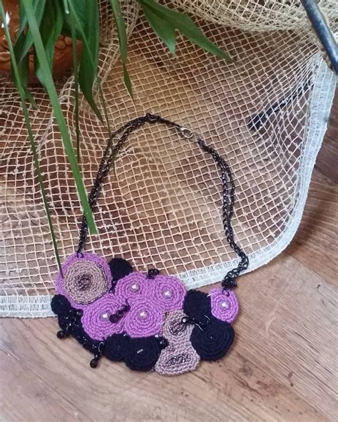 a purple and black crocheted flower necklace on a table next to a potted plant
