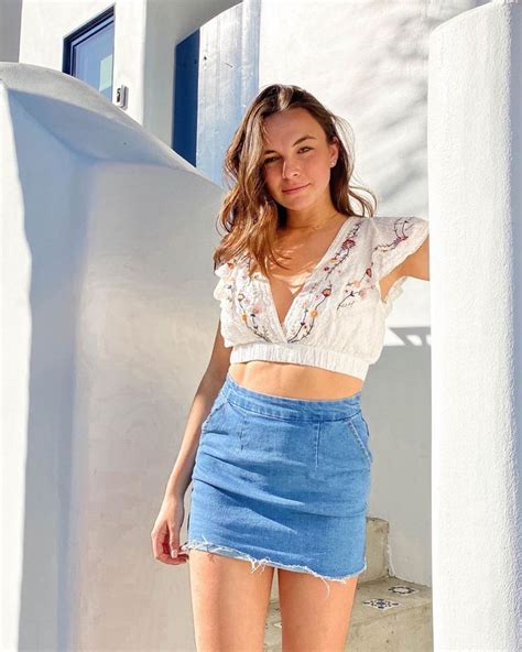 a woman standing in front of a white building wearing a blue skirt and crop top