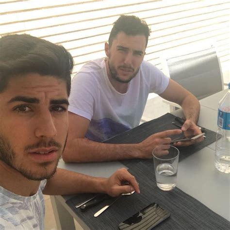two men sitting at a table with cell phones in their hands and water on the table