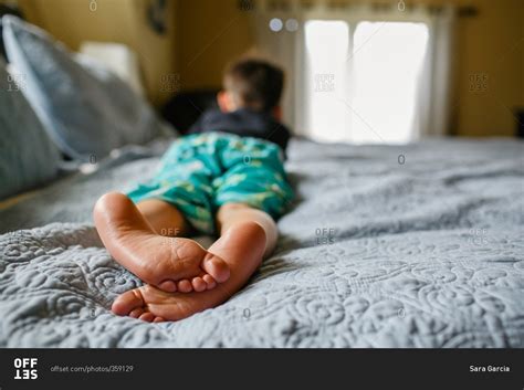 Bare feet of boy lying on bed stock photo - OFFSET