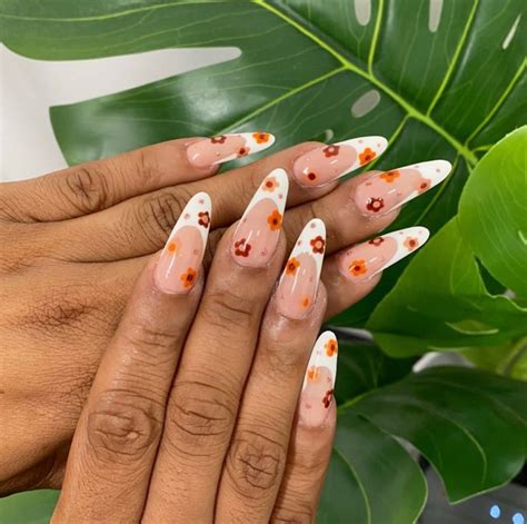 a woman's hand with white and orange nail polish on it, next to a green plant