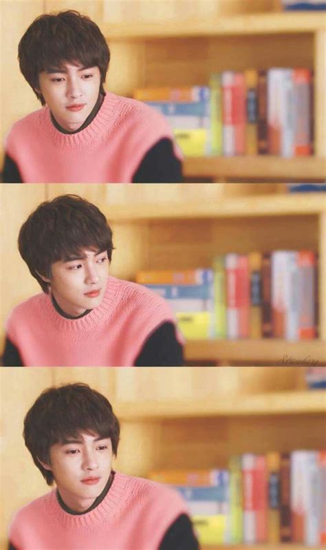 the young man is wearing a pink sweater in front of bookshelves and shelves