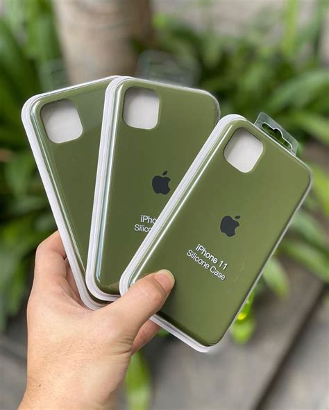 a hand holding three green iphone cases in front of a plant