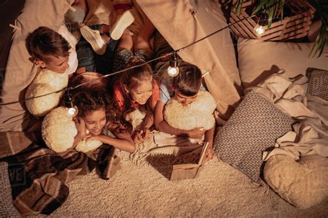 High angle view of multicultural group of children reading book together - Stock Photo - Dissolve