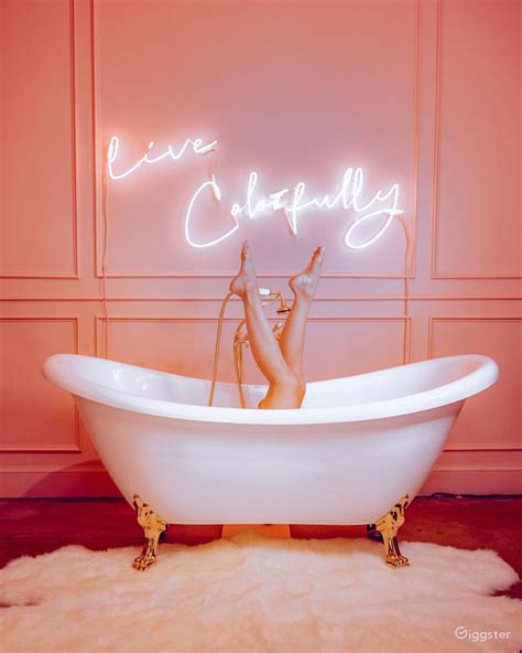 a white bath tub sitting on top of a rug next to a neon sign that reads live happily