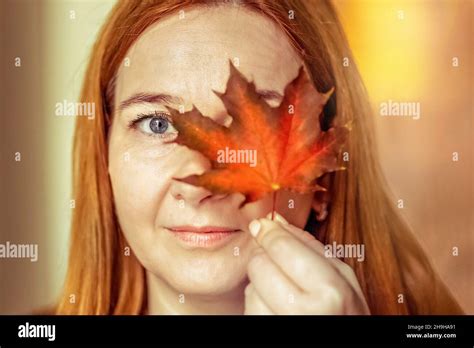 Portrait of a young woman covering one eye with an autumn fallen maple leaf. Autumn mood Stock ...