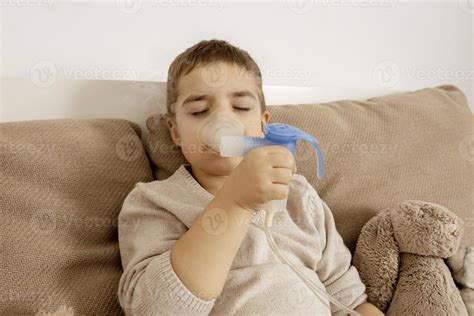 Sick little boy with inhaler for cough treatment. Unwell kid doing inhalation on his bed. Flu ...