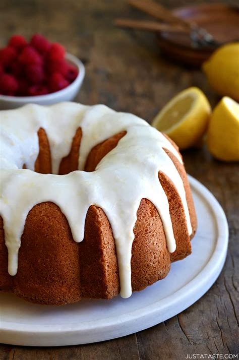 A glazed lemon pound cake on a round, white serving platter with a bowl ...