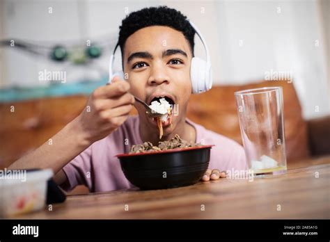Portrait teenage boy with headphones eating at coffee table Stock Photo - Alamy