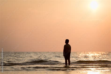 Silhouette of a lonely boy standing alone on the beach at sunset. Concept of lonely and hope of ...