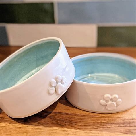 Two ceramic dog bowls. White on the outside with a 3d dog paw on the ...