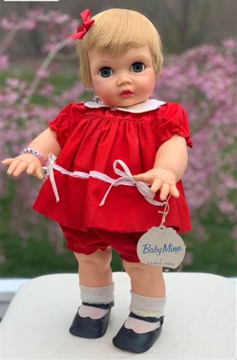 a doll with blonde hair and blue eyes wearing a red dress on a white table
