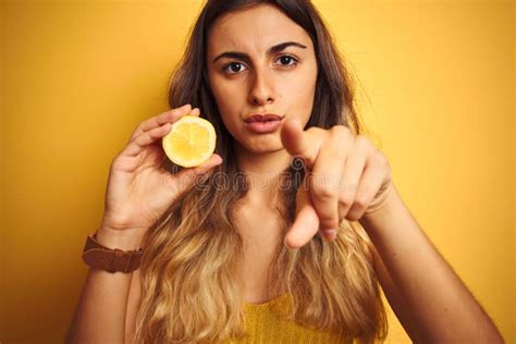 Young Beautiful Woman Holding Half Lemon Over Yellow Isolated Background Pointing with Finger To ...
