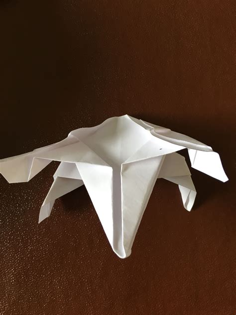 an origami bird sitting on top of a brown table next to a piece of paper