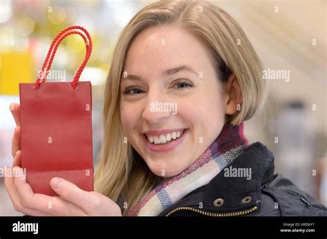 Happy woman displaying a small Christmas gift in a festive red store carrier bag with a warm ...