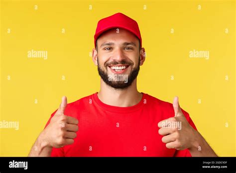 Close-up of friendly smiling delivery guy in red uniform cap and t-shirt provide best express ...