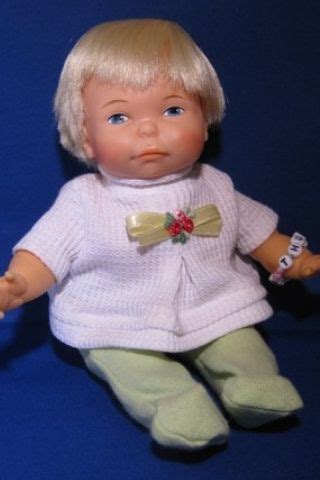 a small doll with blonde hair and blue eyes sitting on a blue background wearing a white sweater ...