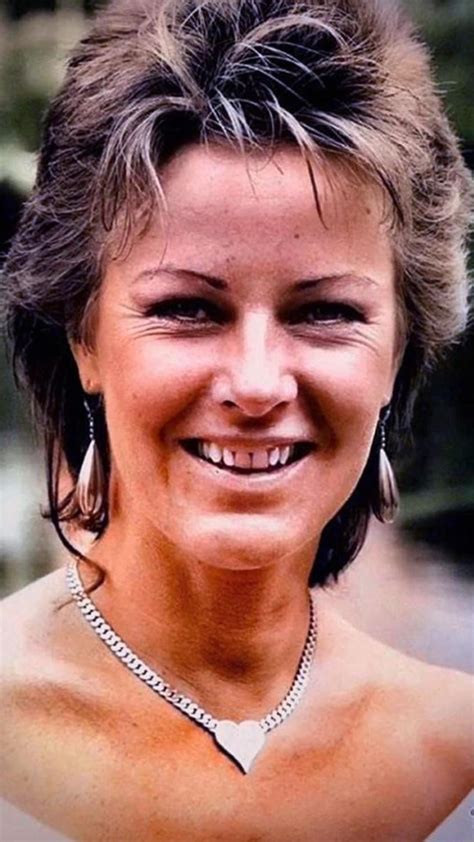 a woman with short hair wearing a necklace and smiling at the camera while standing in front of ...