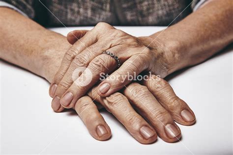 Macro of an old lady sitting with her hands clasped on a table. Elderly woman's hands with a ...