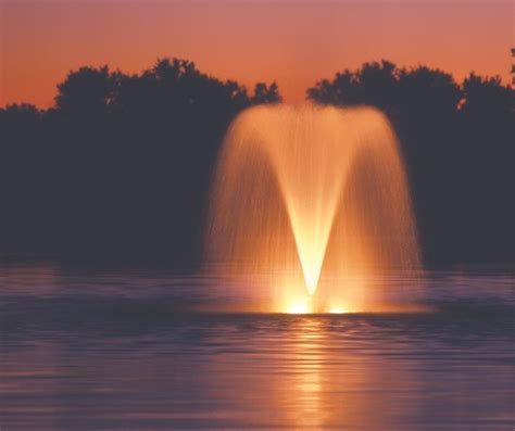 a water fountain in the middle of a lake at sunset