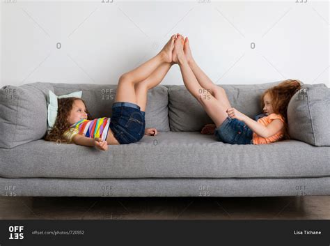 Two girls lying on gray sofa touching feet stock photo - OFFSET