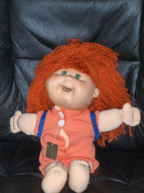 a small doll with red hair sitting on a black leather chair and smiling at the camera