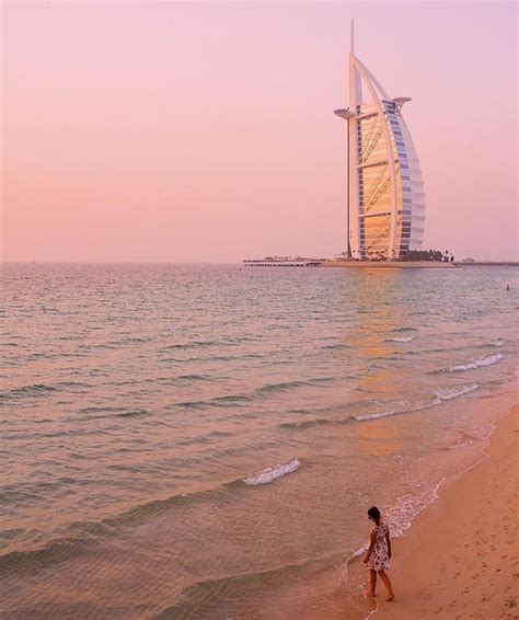 a person walking on the beach in front of an ocean with a tall building ...