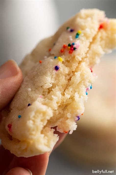 a hand holding a half eaten sugar cookie with sprinkles