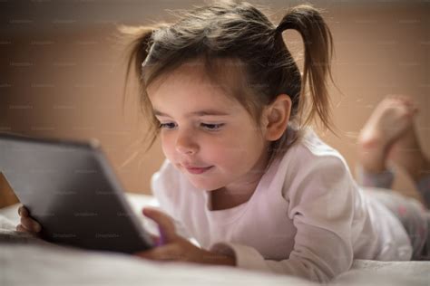 She wants to see the digital world before dreamland. Little girl using digital tablet in bed ...