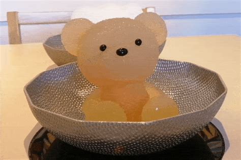 a teddy bear sitting in a metal bowl on a counter top with bubbles coming out of it