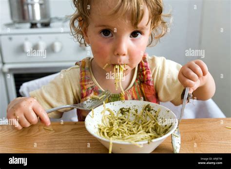 A young girl eating pasta with pesto at the kitchen table Stock Photo - Alamy