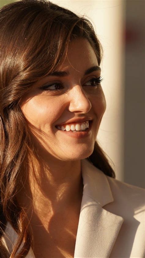 a close up of a woman smiling and wearing a white suit with her hair in a pony tail
