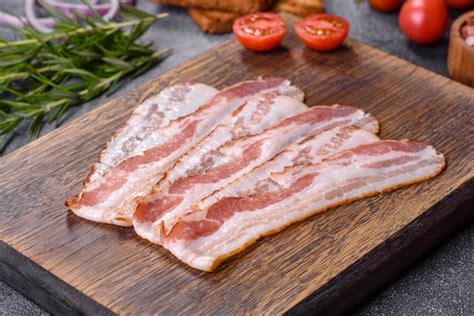 Premium Photo | Raw smoked bacon slices on a wooden board with spices ...