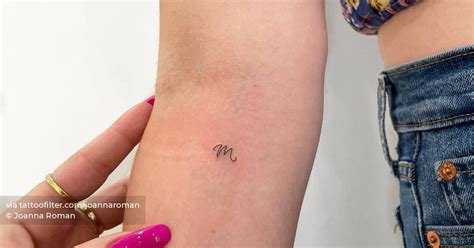 Tiny letter "M" tattoo located on the inner forearm.