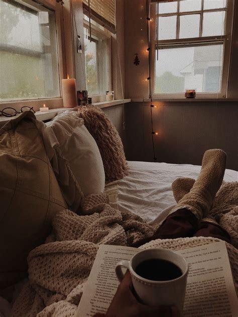 a person laying in bed reading a book and holding a cup of coffee