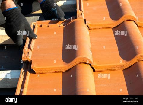 Closeup of worker hands installing yellow ceramic roofing tiles mounted ...