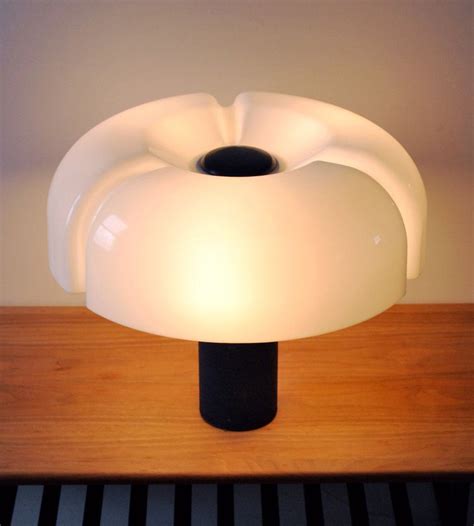 a white lamp sitting on top of a wooden table next to a black pole and wall